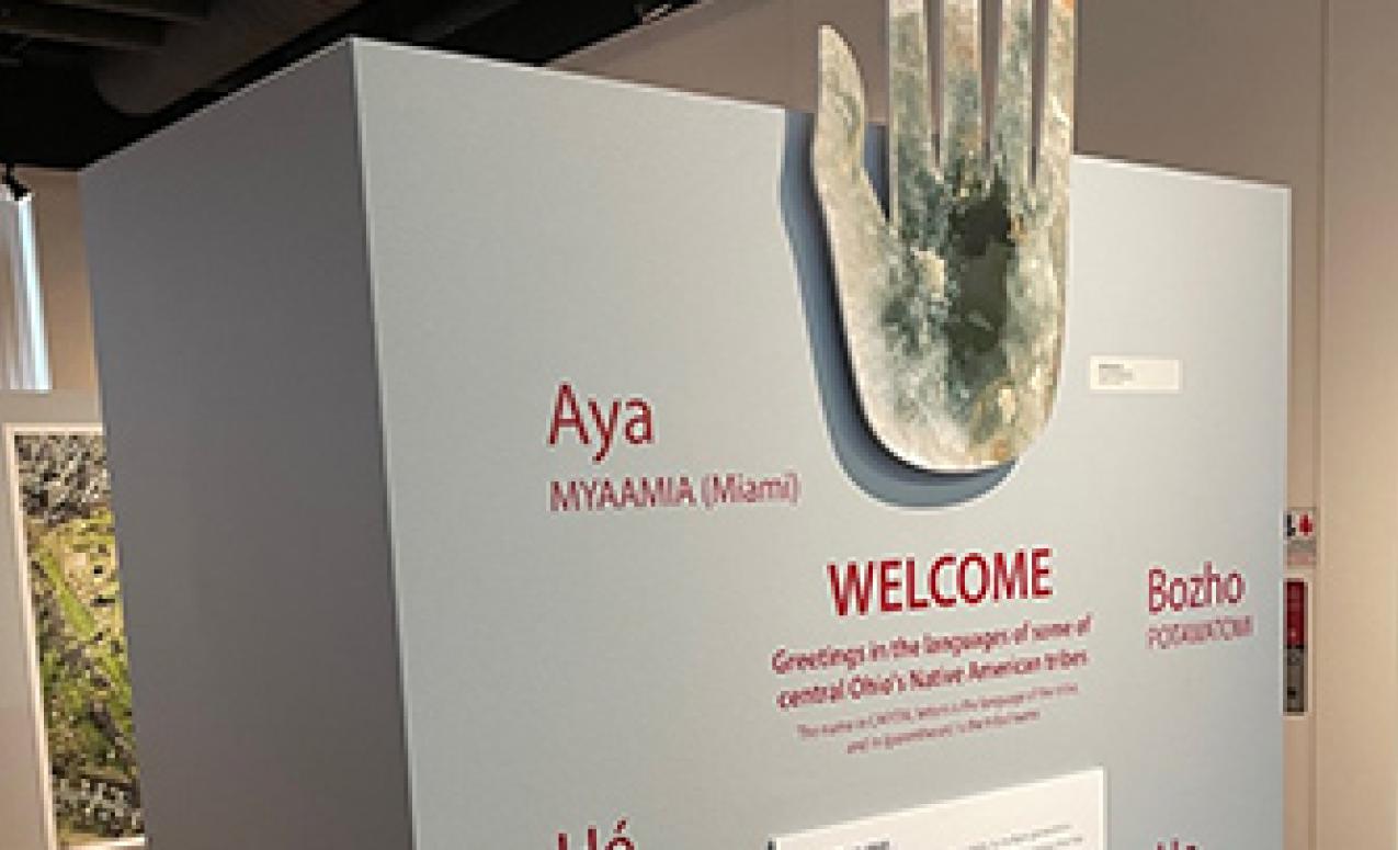 Welcome to Mounds, Moon and Stars: The Legacy of Ohio's Magnificent Earthworks Art Exhibit. The Works, Newark Ohio. Mica hand above grey plinth with welcome in Ohio's indigenous languages.