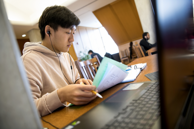 Student with earbuds in, with study materials and laptop in a quiet study space. Image courtesy of The Ohio State University.