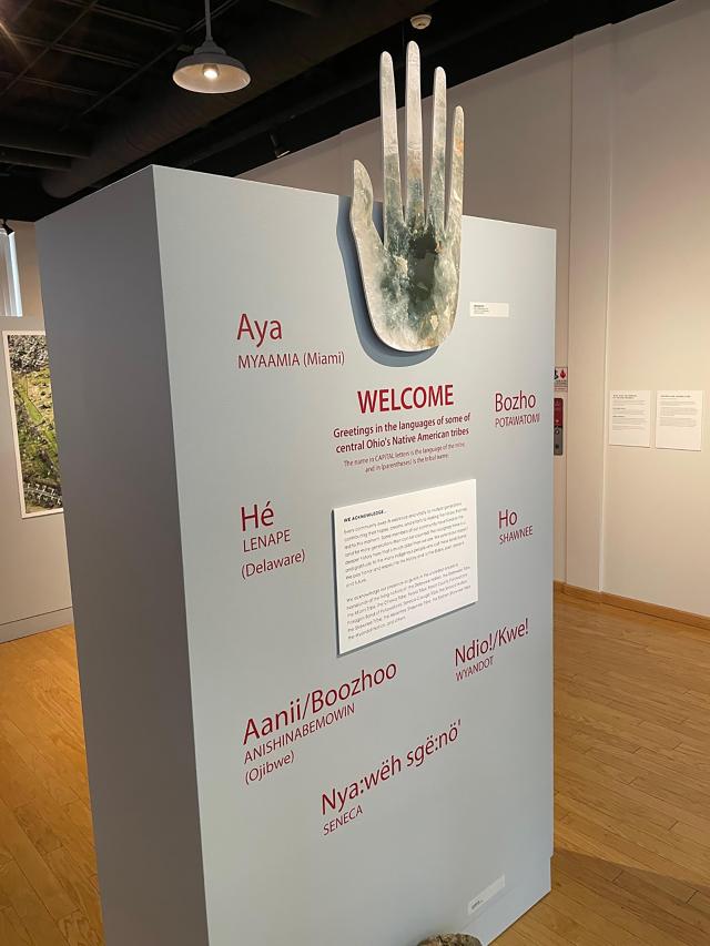 Welcome to the Mounds, Moon and Stars: The Legacy of Ohio's Magnificent Earthworks Art Exhibit. The Works, Newark Ohio. Mica hand above grey plinth with welcome in Ohio's indigenous languages.