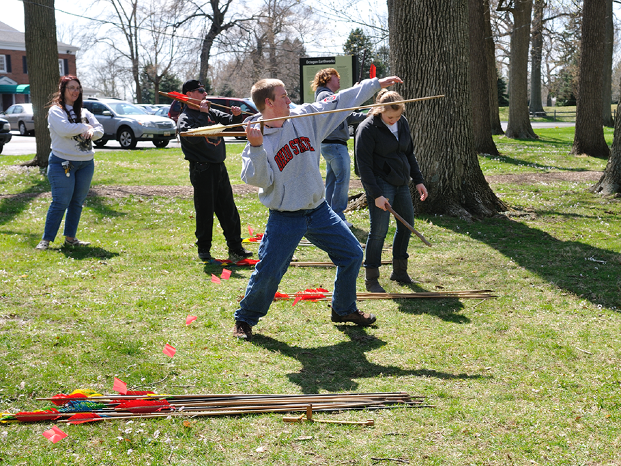 Students in mid-motion of throwing an atlatl [an assistive tool for spear throwing] at the Octagon State Memorial, Newark.