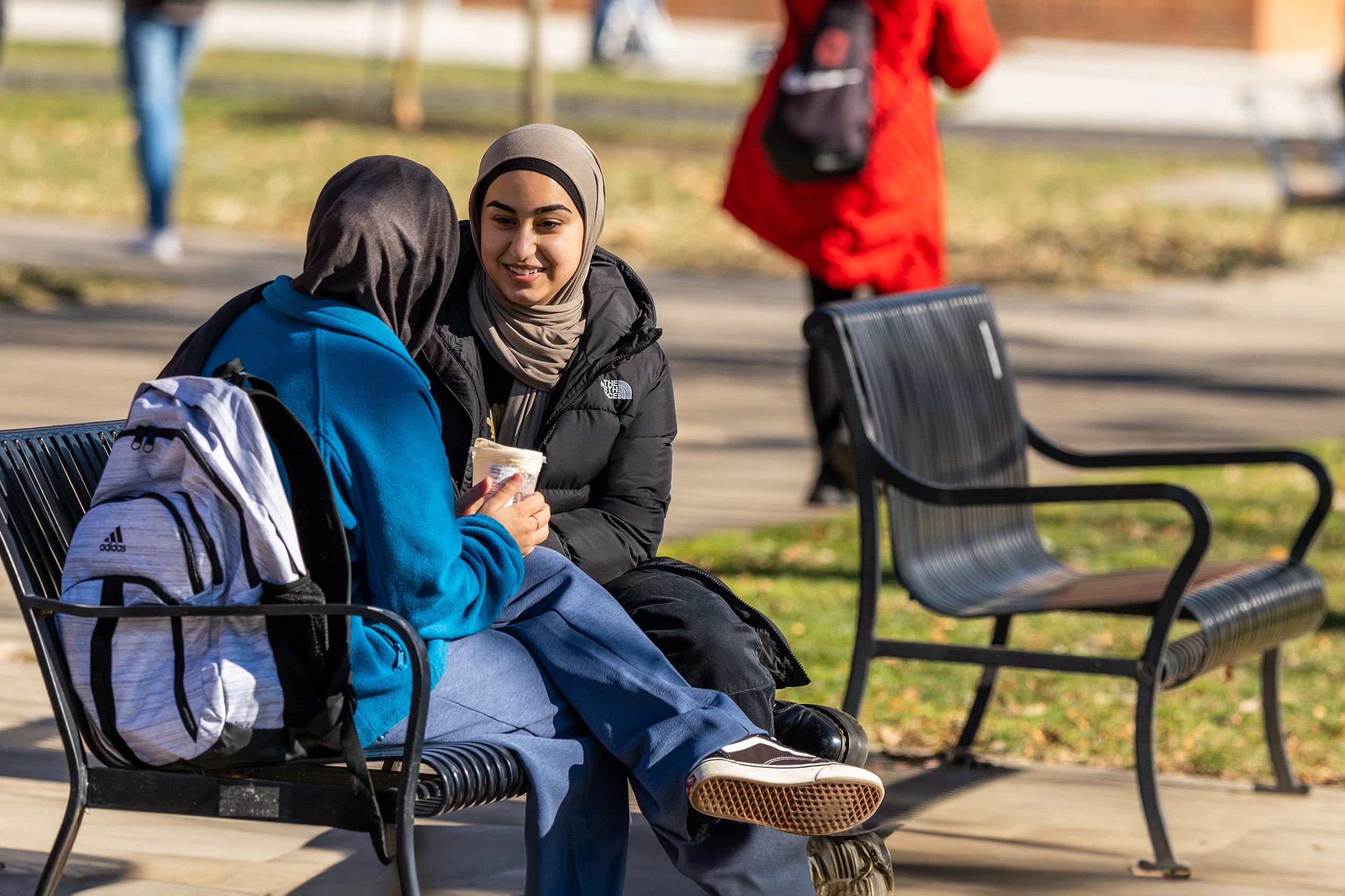 Two students talking on a bench on campus