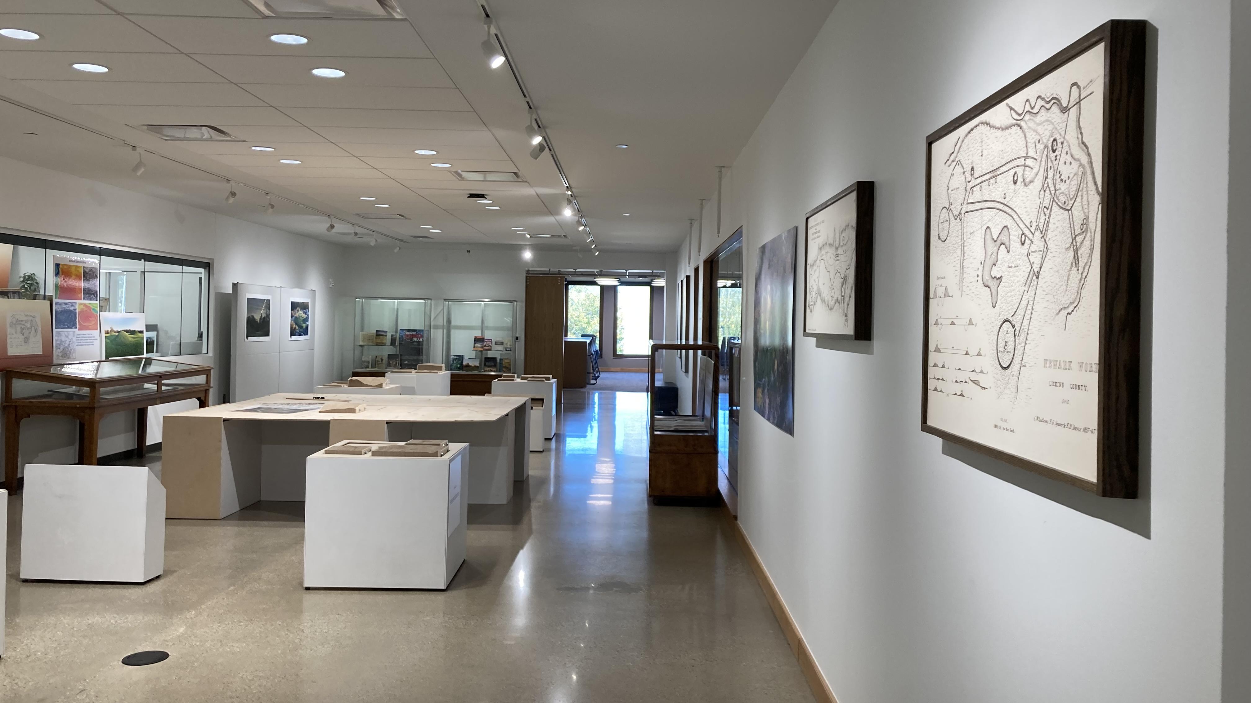 Long view of the Newark Earthworks Storyteller's Gallery showing framed earthworks maps on the wall, an interactive wood map table to the left and wooden file boxes with earthworks maps hanging.