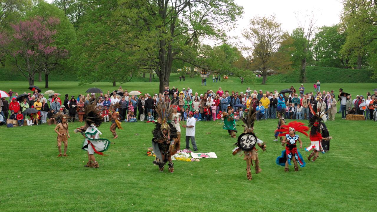 Aztec dancers dancing while a crowd watches behind them with the Newark Earthworks around them.