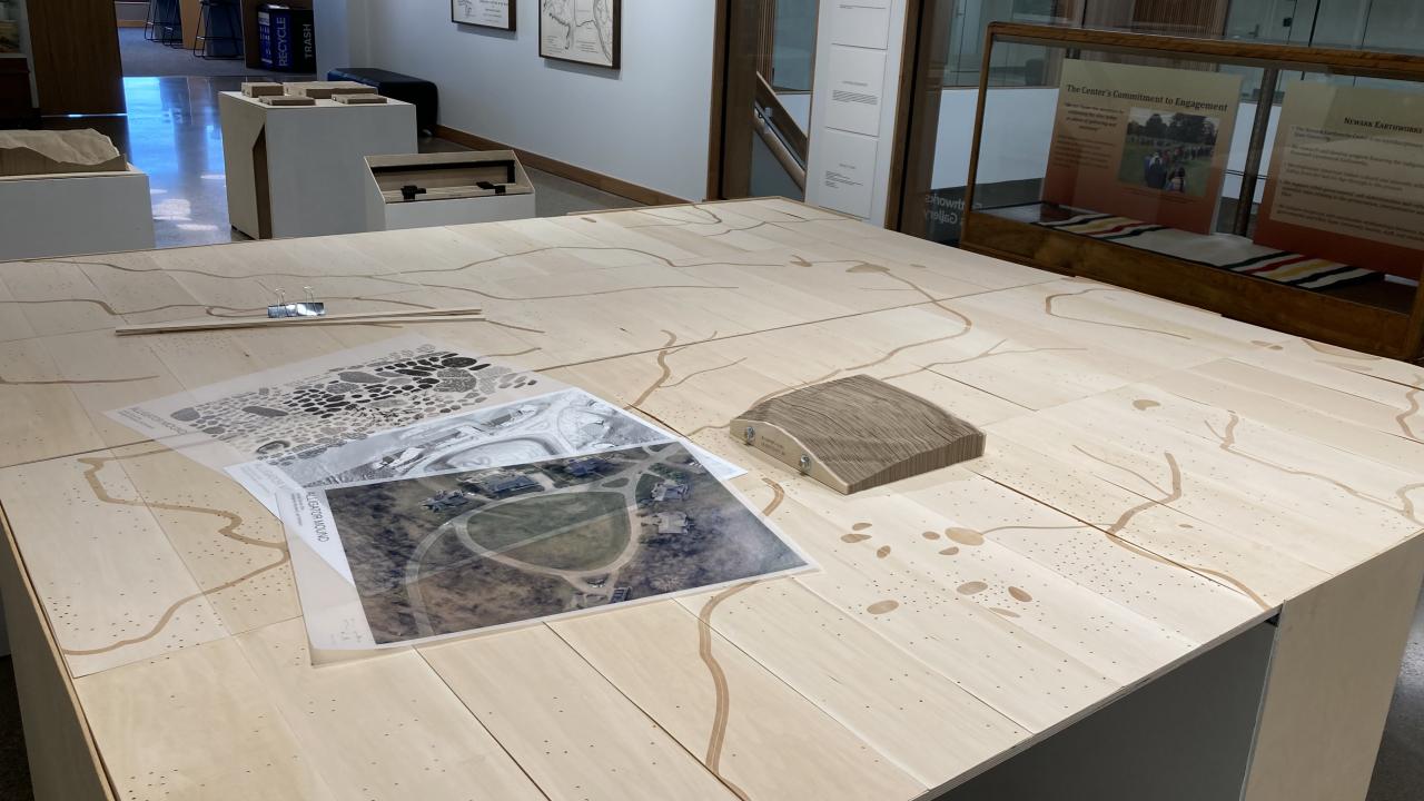 Close-up of interactive map of Ohio river valleys with dots representing existing indigenous earthworks sites. Drawings, map, and survey of a specific earthworks lays on the table.